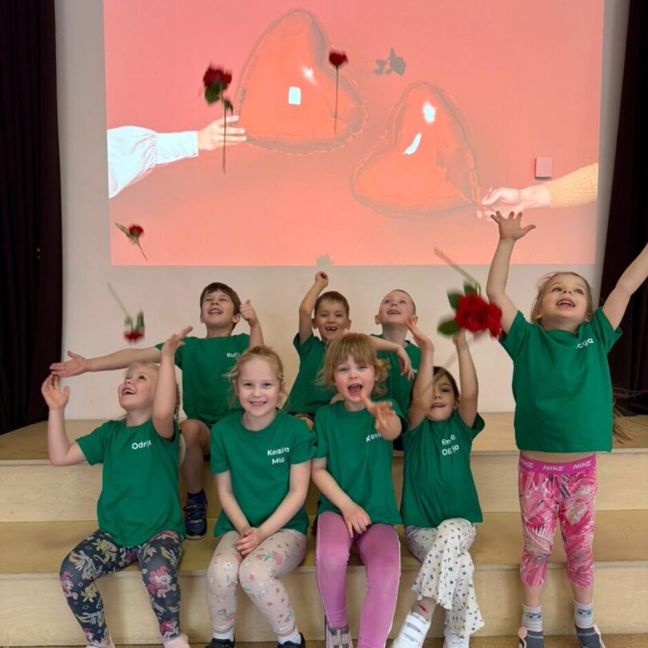 Priecīgi bērni zaļos krekliņos, rozes. Fonā ekrāns ar sirdīm.