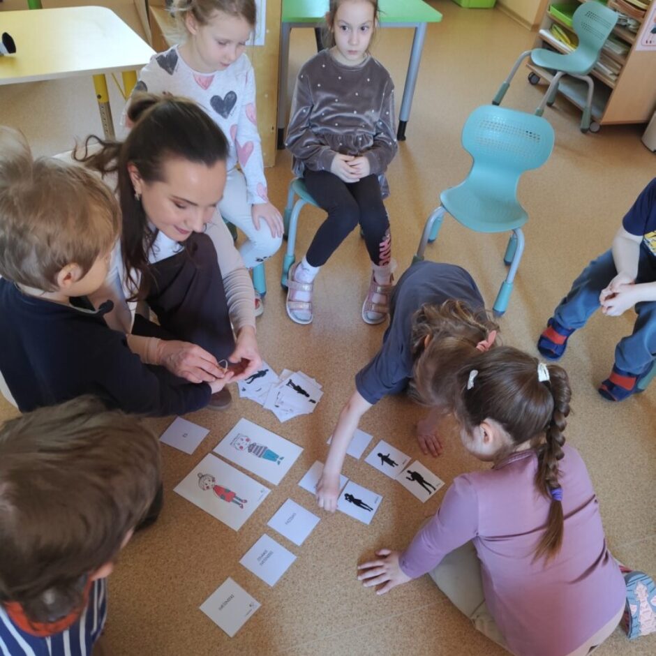 Skolotāja, bērni, Džimbas lelle. Grupas iekārtojums fonā.