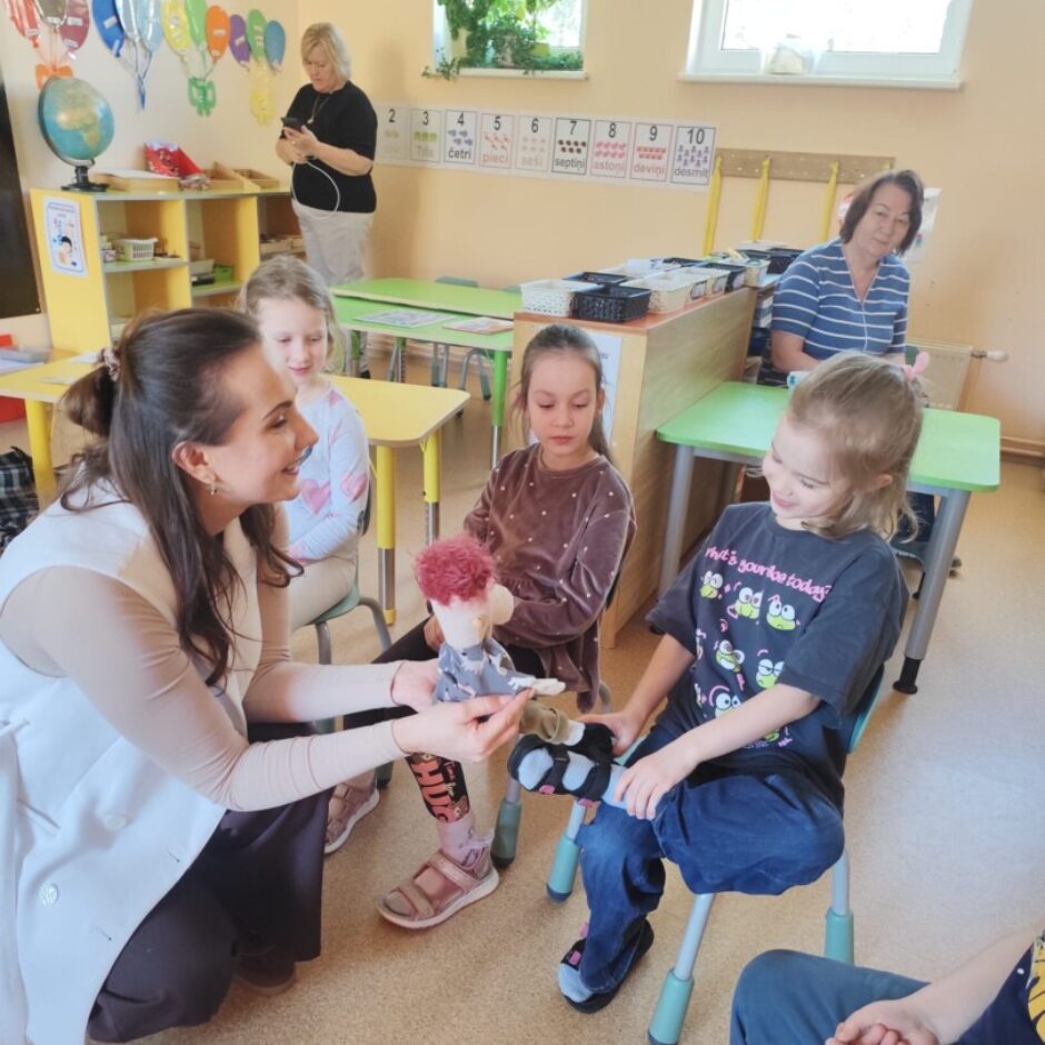 3 skolotājas, bērni, Džimbas lelle. Grupas iekārtojums fonā.