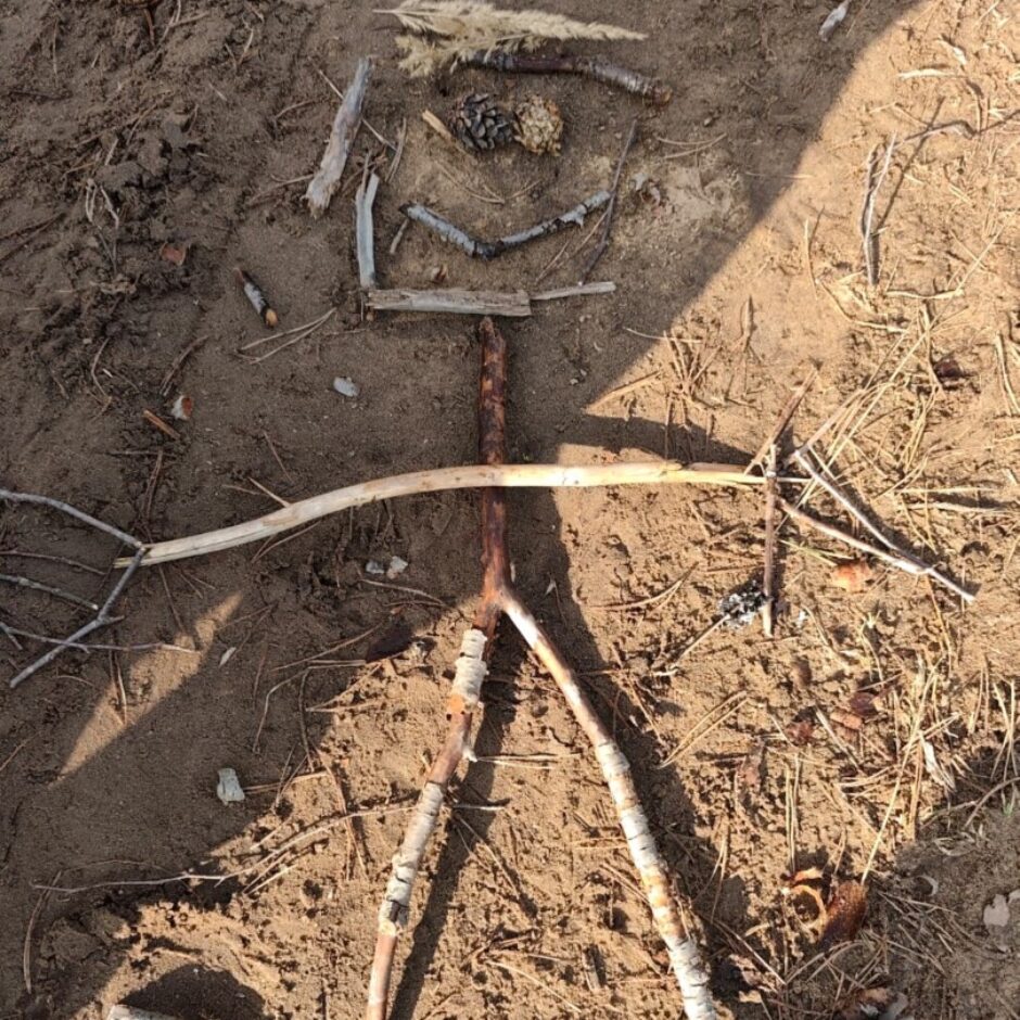 Uz brūnas zemes no kociņiem un čiekuriem izlikts cilvēks.