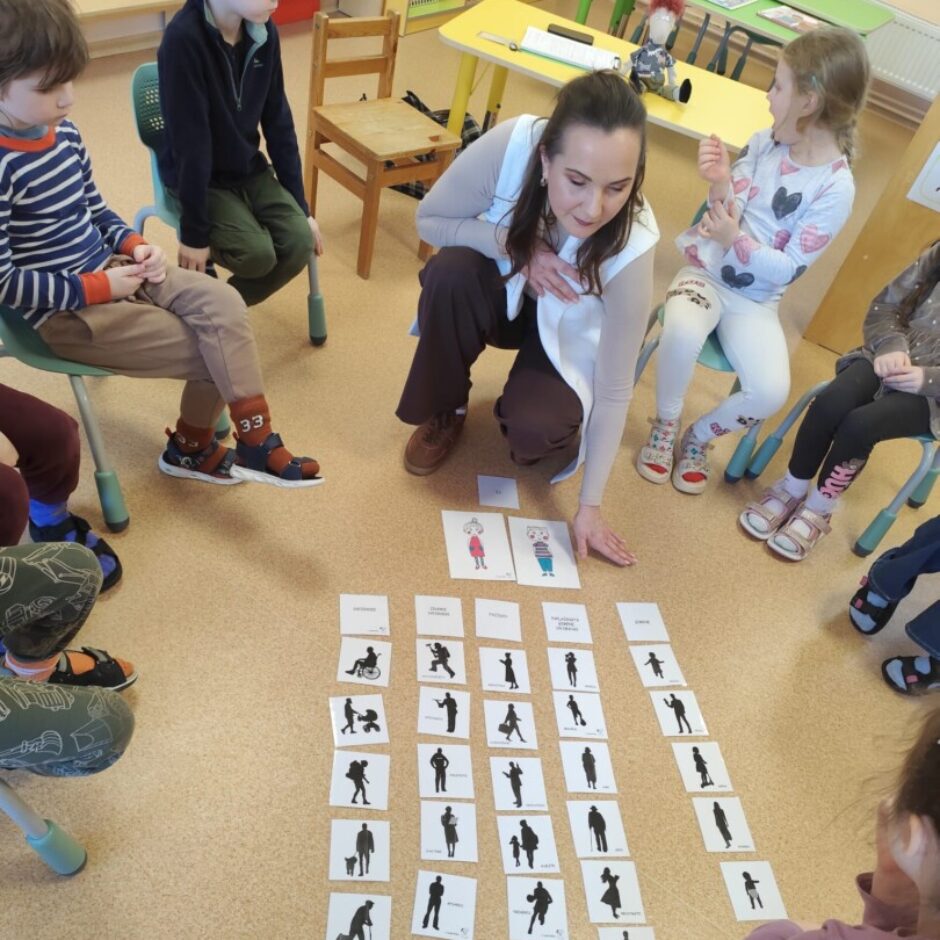 Skolotāja izlikusi uz brūna grīdas seguma dažādus melnbaltus attēlus.