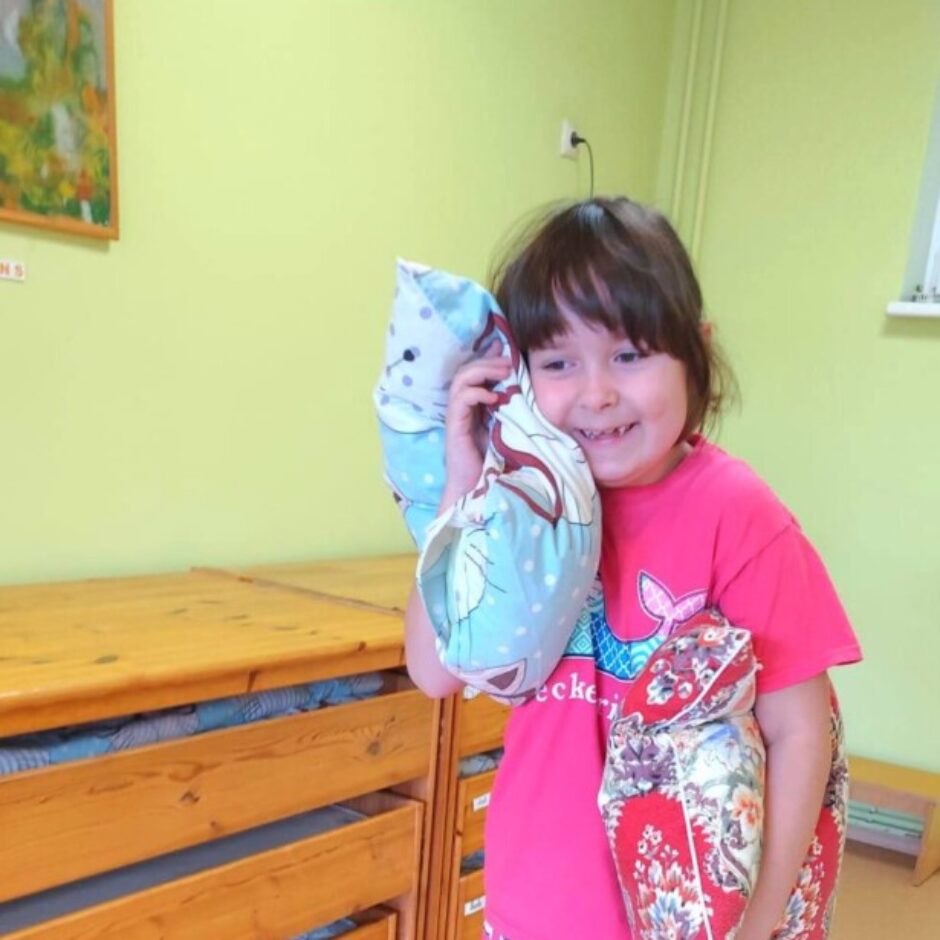 Smaidoša meitene ar tumšiem matiem, tērpusies rozā T-kreklā ar uzrakstu 