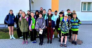 Grupas foto ar jauniešiem un vienu vīrieti ārā, daudziem ap kaklu ir bronzas medaļas. Viņi ir ģērbušies ikdienas un sporta apģērbā. Vīrietis ar bārdu stāv aizmugurē.