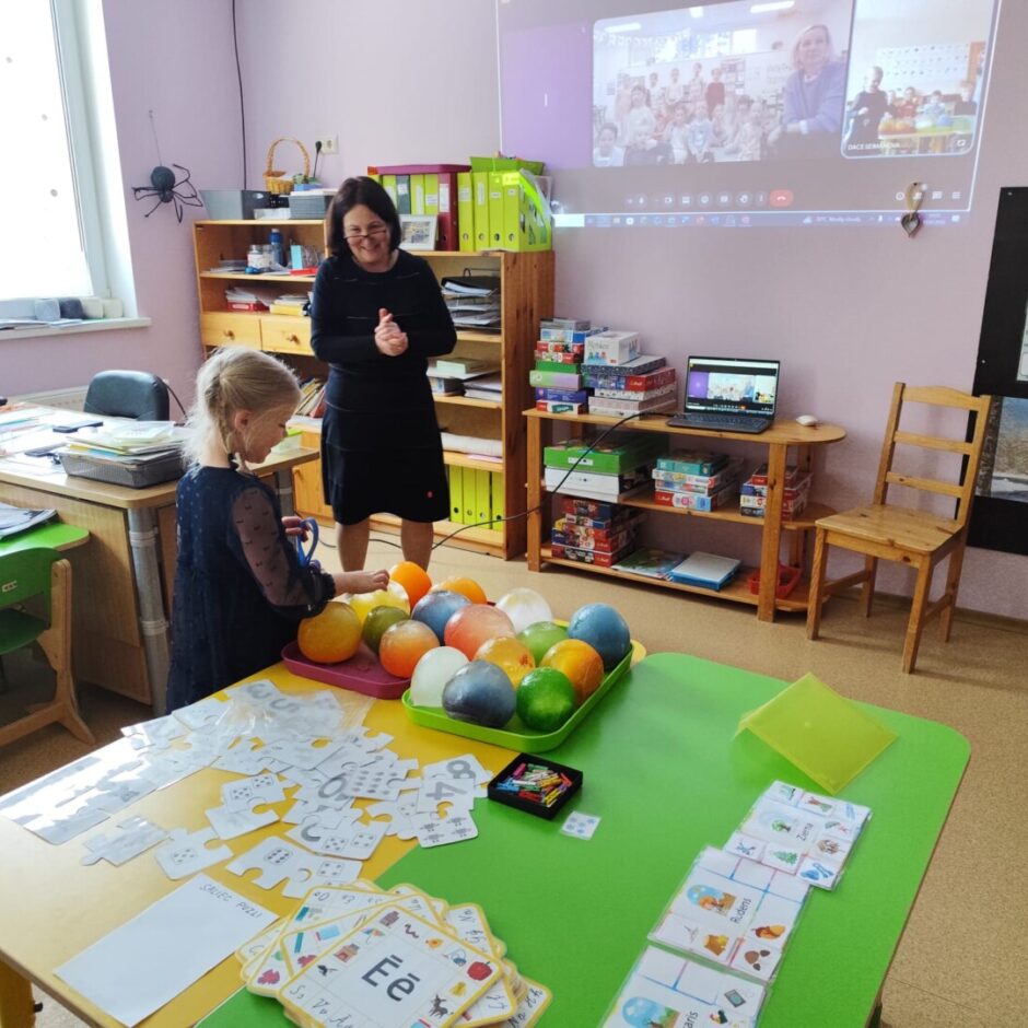 Skolotāja, bērns, uz zaļa un dzeltena galda krāsainas ledus bumbas. Fonā Sprīdīšu grupas iekārtojums - plaukti, galdi, spēles.